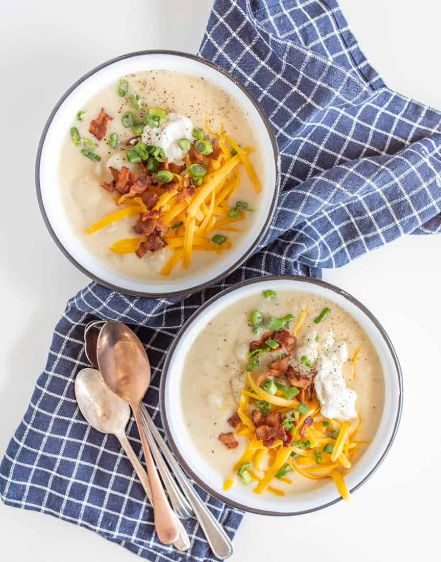 A top view of two bowls of potato soup topped with cheese, green onions, sour cream, and cheddar cheese.