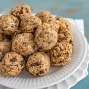 balls of oats, peanut butter, chocolate chips, and other ingredients on a white plate set on a white and white towel.