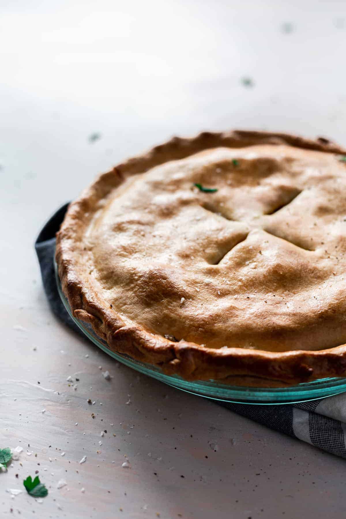 golden brown pie with four holes cut into top in a glass pie pan.