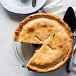 top view chicken pot pie in a clear pie pan with a golden crust and once slice taken out