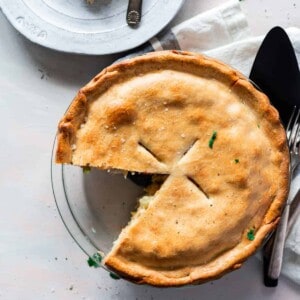 top view chicken pot pie in a clear pie pan with a golden crust and once slice taken out