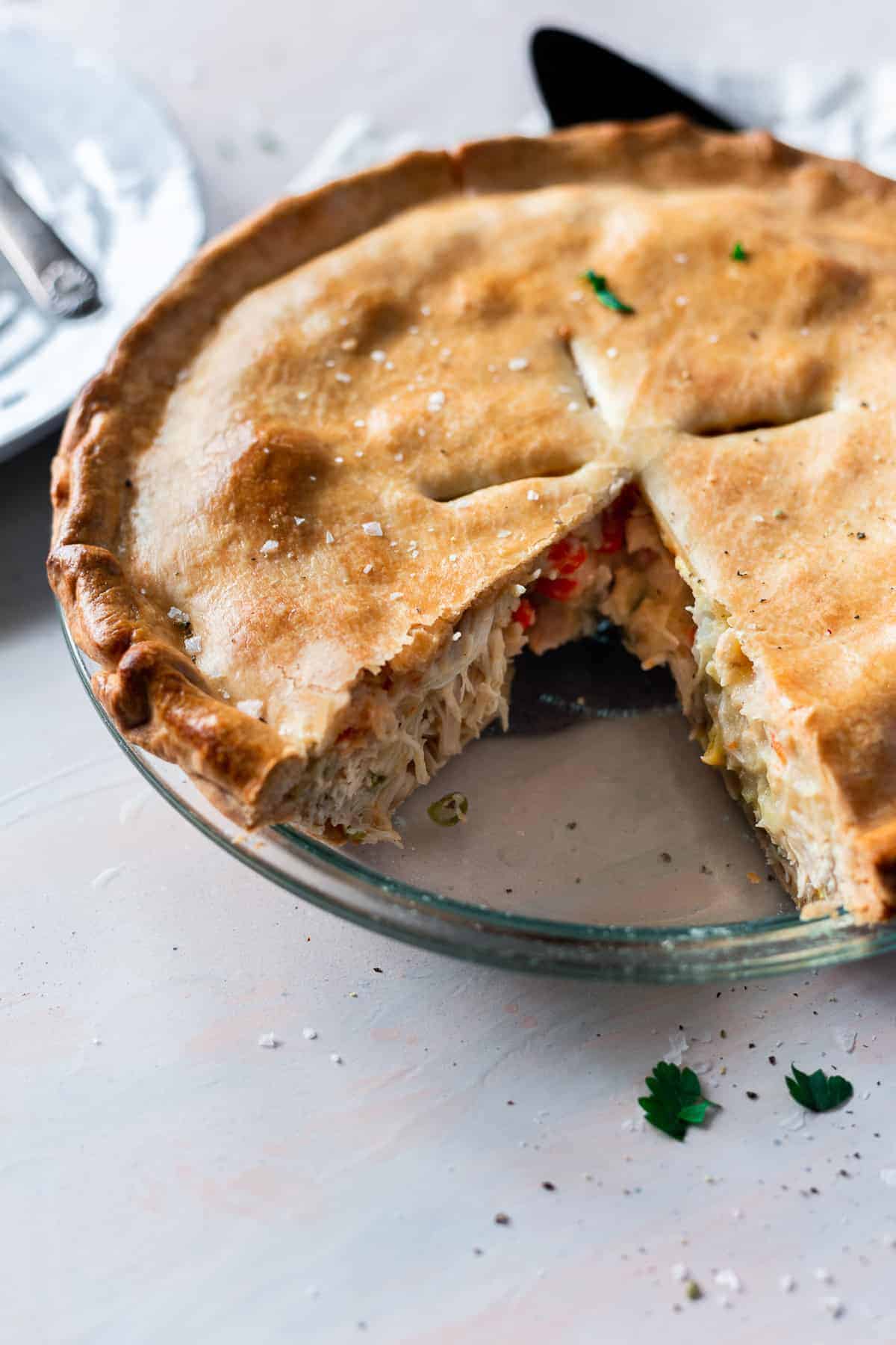 baked pie crust filled with chicken, corn, peas, and carrot mixture in a pie pan with a slice cut gone.