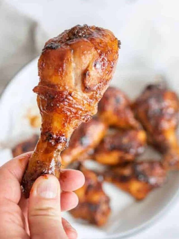 a hand holding a saucy baked chicken leg