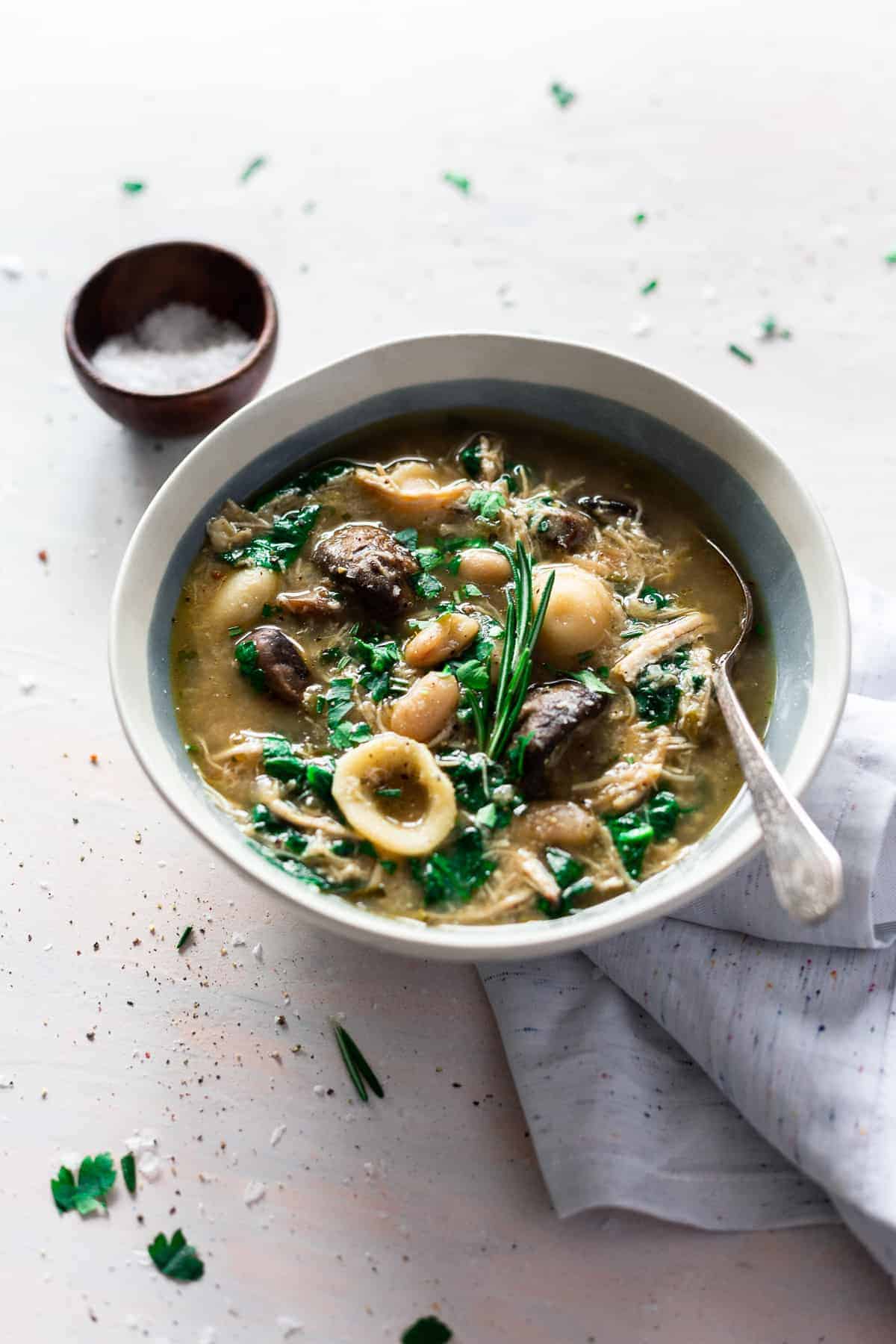 soup with pasta, mushrooms and chicken in a white and blue bowl salt in a bowl in background.