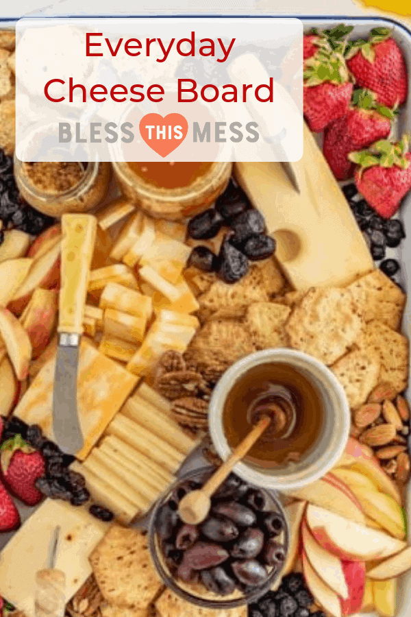 Title Image for Everyday Cheese Board with a variety of cheeses, crackers, olives, fruit, nuts, and spreads arranged on a serving tray