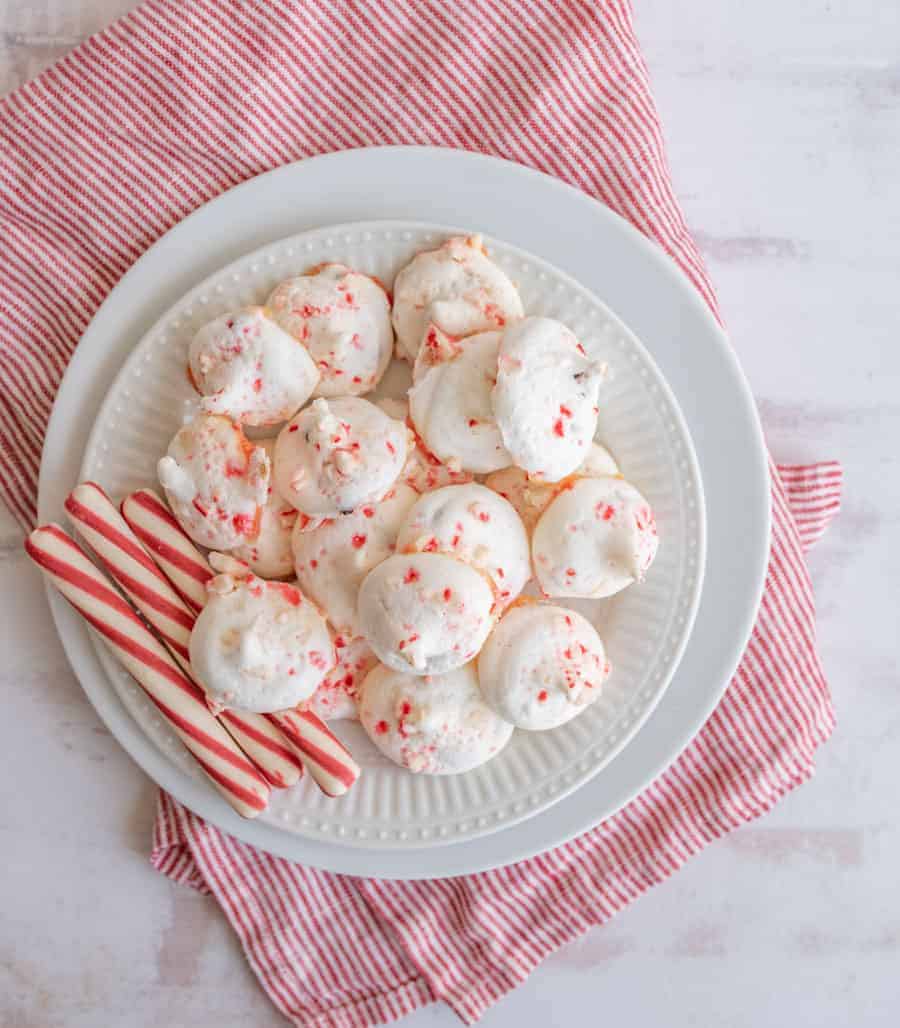 White plate with candy cane meringue cookies piled beside peppermint sticks.