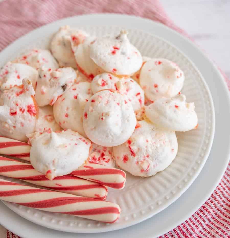 White plate with candy cane meringue cookies piled beside peppermint sticks.