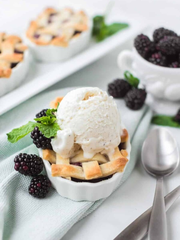 small white dishes filled with blackberry pie filling and a lattice crust with blackberries all around and vanilla ice cream