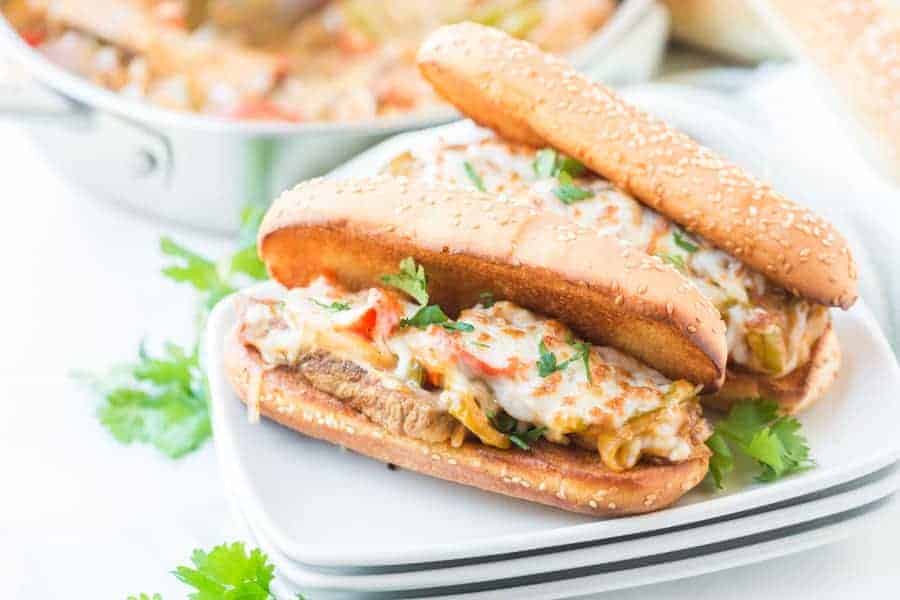 Toasted hoagie bun filled with steak, peppers, onions and cheese on white plate, garnished with parsley.