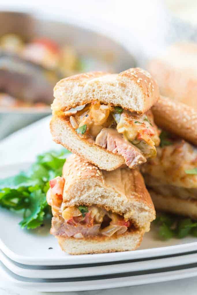 sesame bun stuffed with melty classic cheesesteak ingredients with parsley on a stack of three white plates