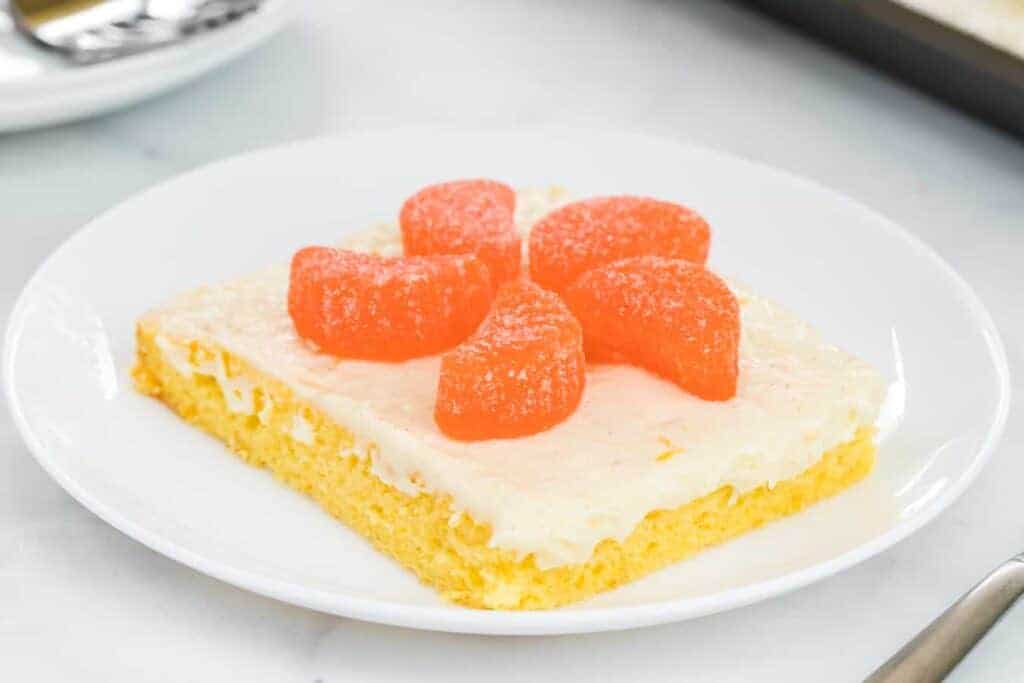 thin orange cake slice with white icing and orange candies on top