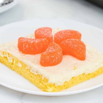 thin orange cake slice with white icing and orange candies on top