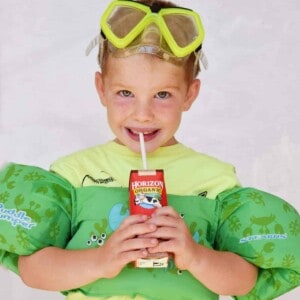 little boy drinking horizon chocolate milk with pool floats and goggles on