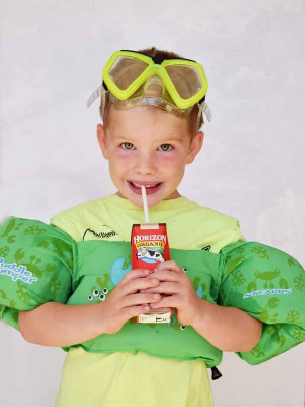 little boy drinking horizon chocolate milk with pool floats and goggles on