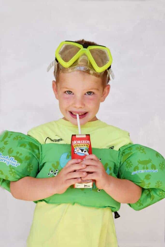 little boy drinking horizon chocolate milk with pool floats and goggles on