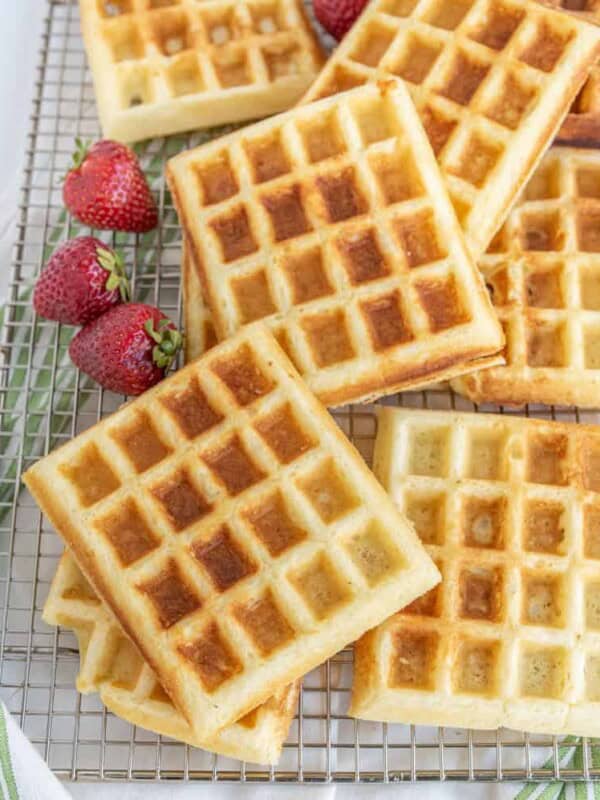 buttermilk waffles on a plate with syrup and strawberries on a cooling rack.