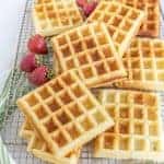 buttermilk waffles on a plate with syrup and strawberries.