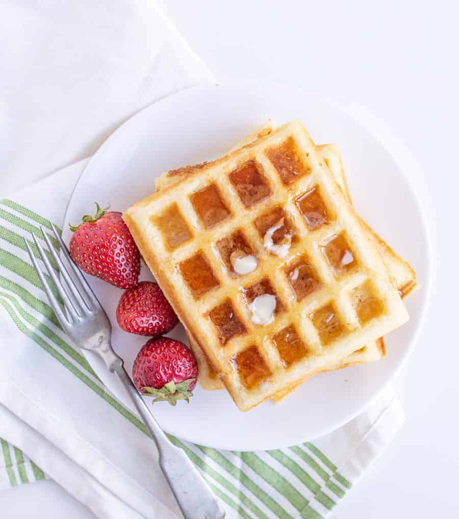 waffles on a plate with syrup and strawberries.