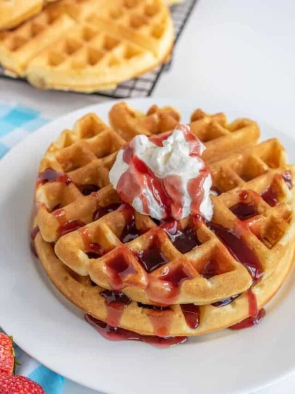 a stack of homemade waffles with whipped cream and syrup