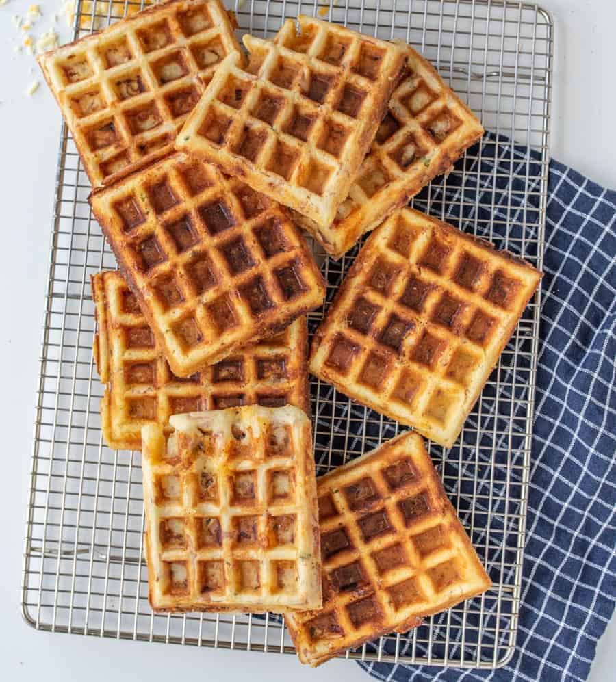 Golden-brown waffles stacked on a cooling rack, with a scoop of creamy ice cream perfectly melting beside them on a blue and white checkered cloth.