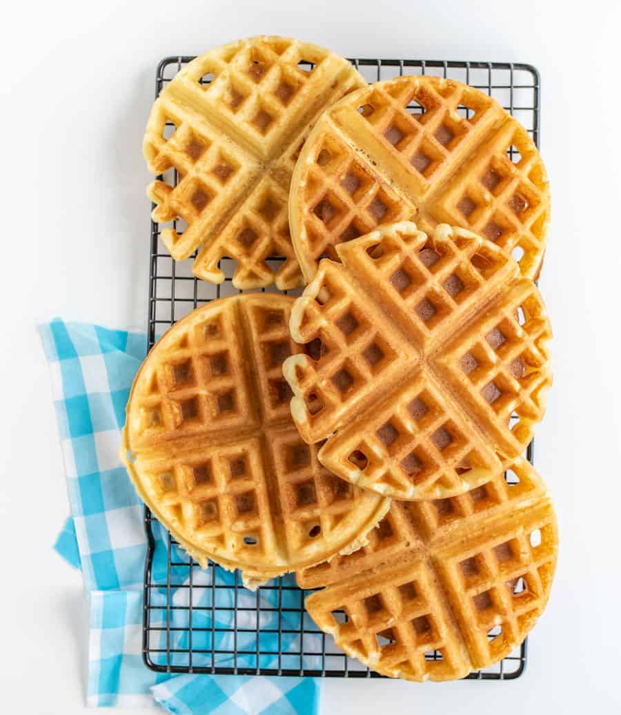 Several waffles stacked on a black wire rack with blue and white towel underneath.