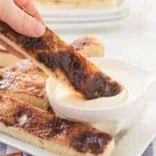 cinnamon stick bread on a white plate with a small dish of icing