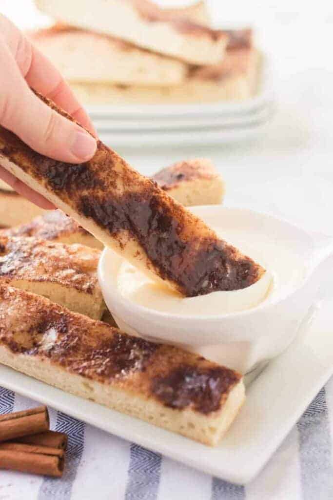 cinnamon stick bread on a white plate with a small dish of icing