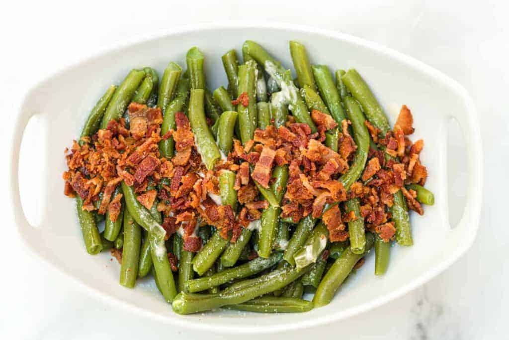 green beans on a white plate with bacon on top
