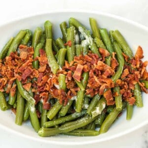 A white oval dish filled with Green Beans with Butter and Bacon, the tender beans cooked to perfection and topped with chopped crispy bacon pieces.