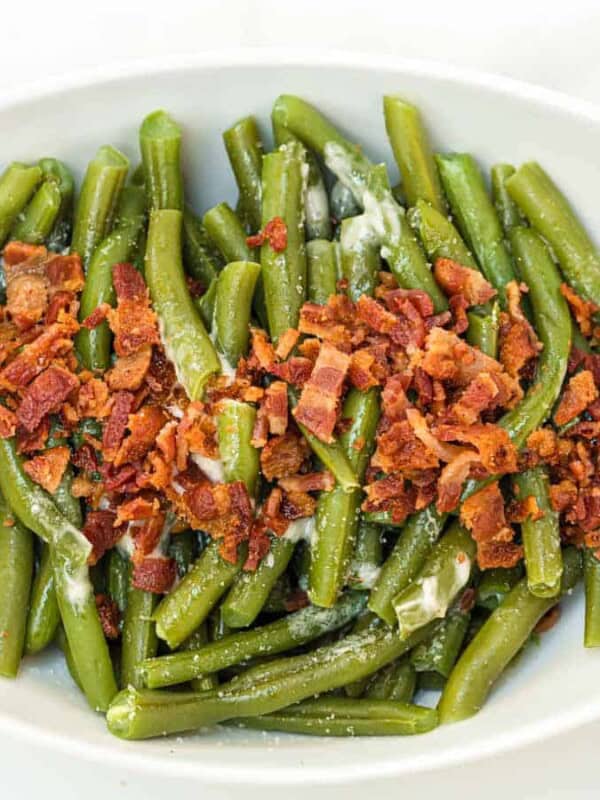 green beans on a white plate with bacon on top