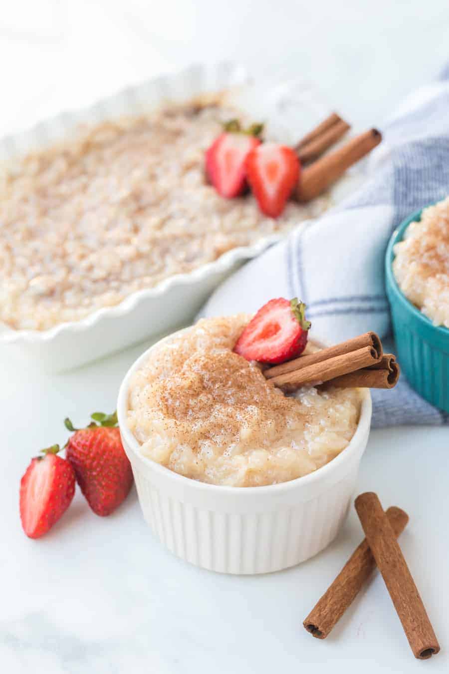 creamy pudding in white ramekin with strawberries and cinnamon sticks.