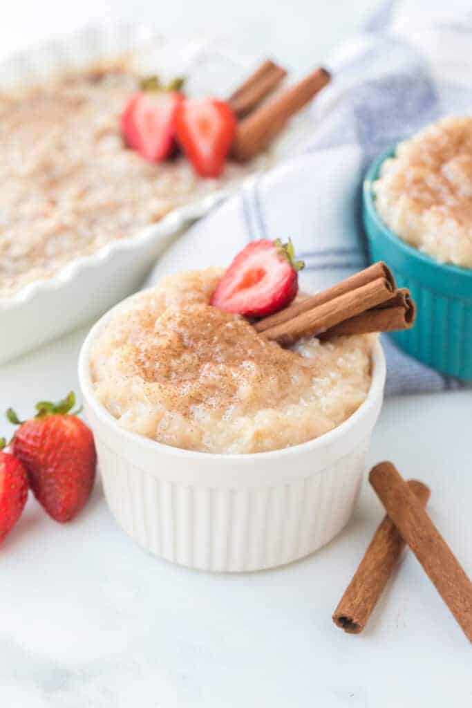 Rice pudding in white ramekin with strawberries and cinnamon sticks