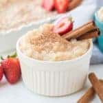 Rice pudding in white ramekin with strawberries and cinnamon sticks