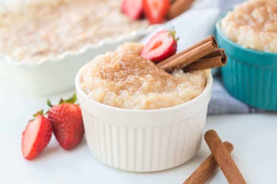 Rice pudding in white ramekin with strawberries and cinnamon sticks