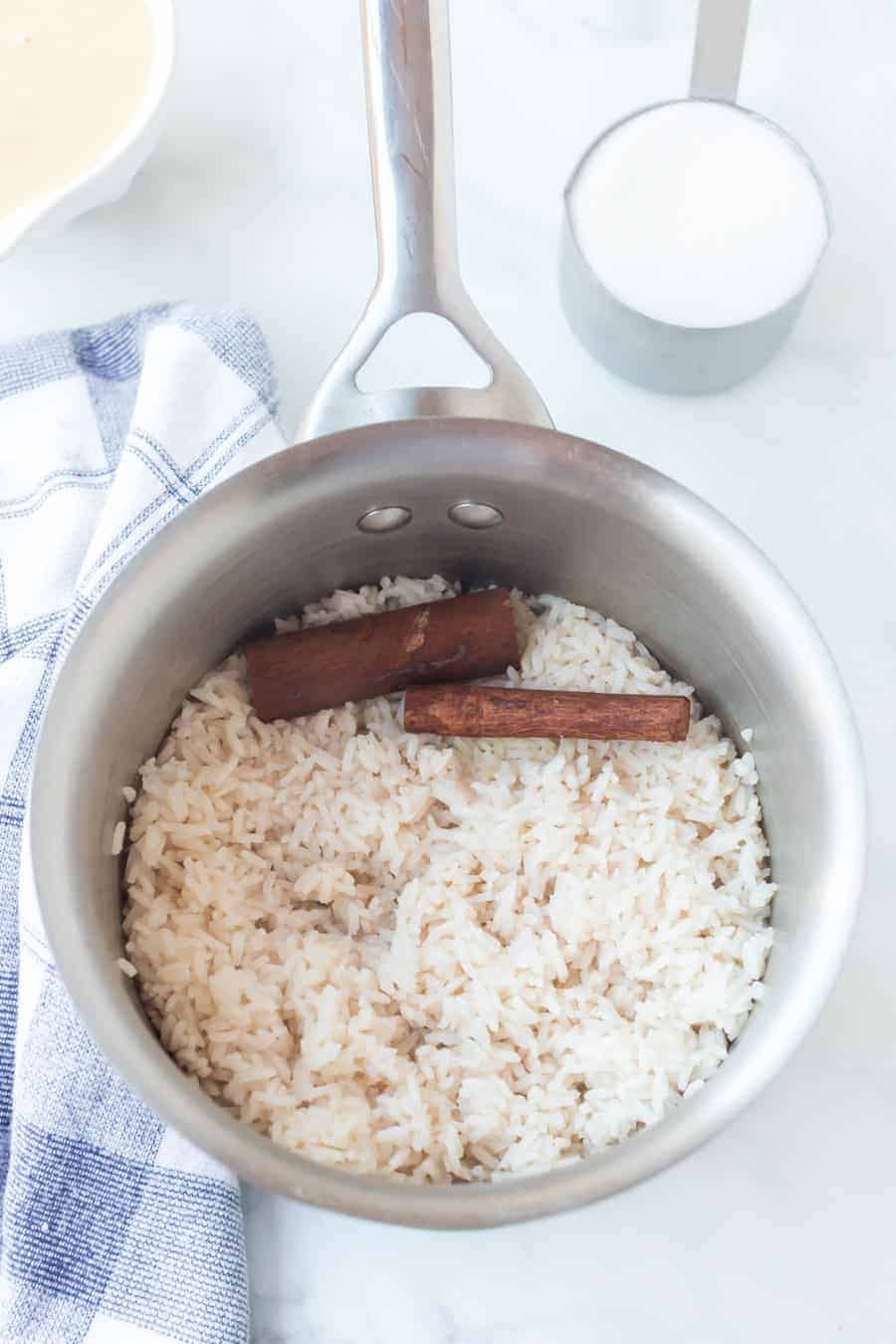 white rice with cinnamon sticks in medium sauce pan on blue checkered towel