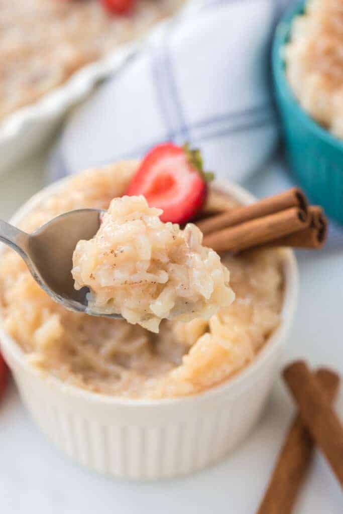 Rice pudding in white ramekin with strawberries and cinnamon sticks