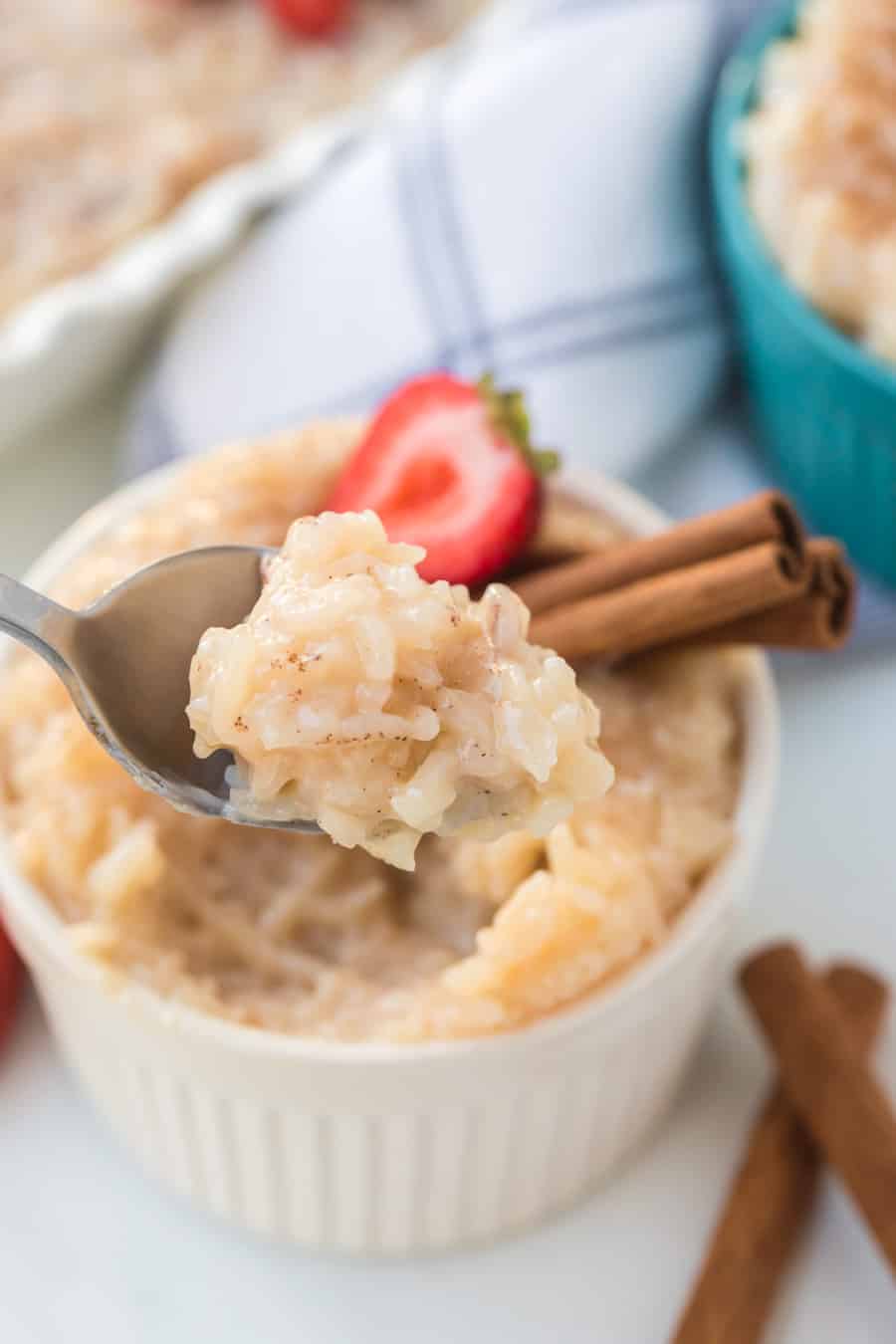 Rice pudding with strawberries and cinnamon sticks in white ramekin with spoon