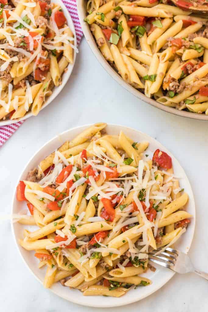 pene pasta with shredded cheese with tomatoes and herbs on a white plate