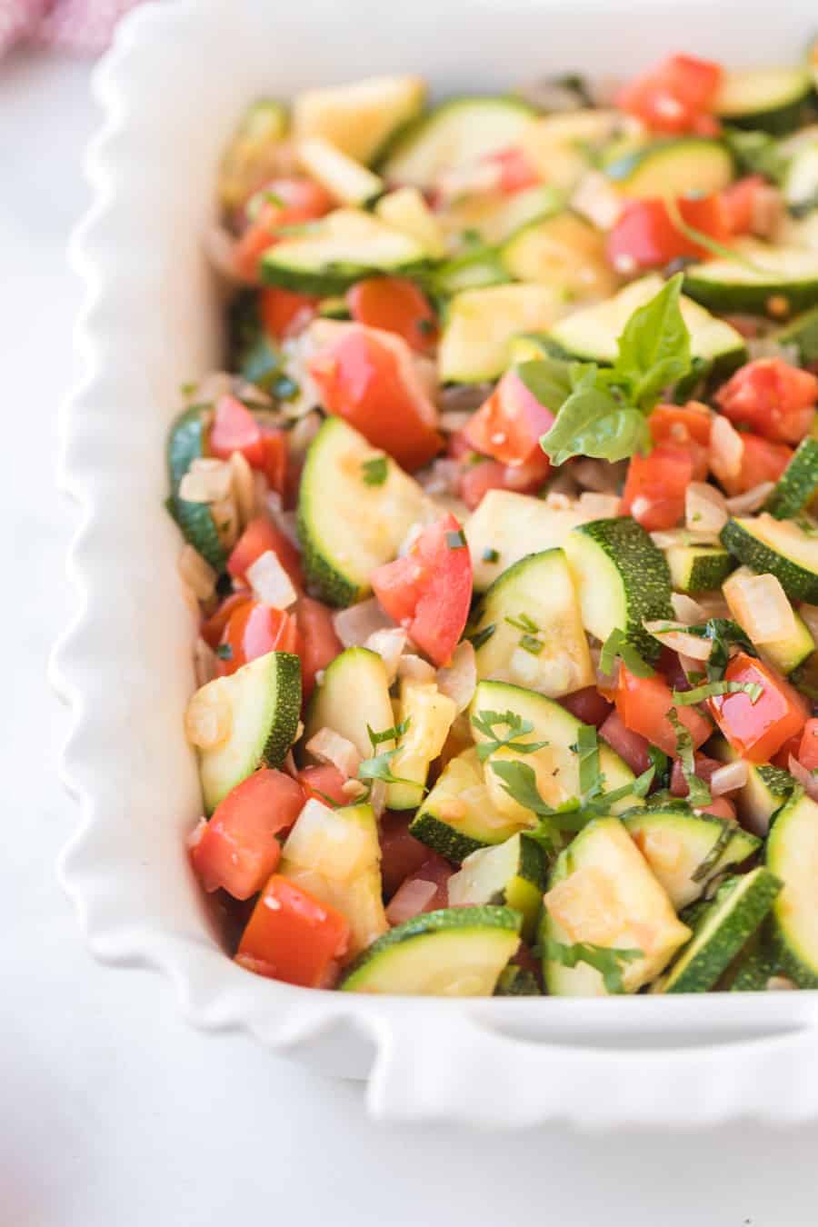 zucchini and tomato side dish in a white dish.