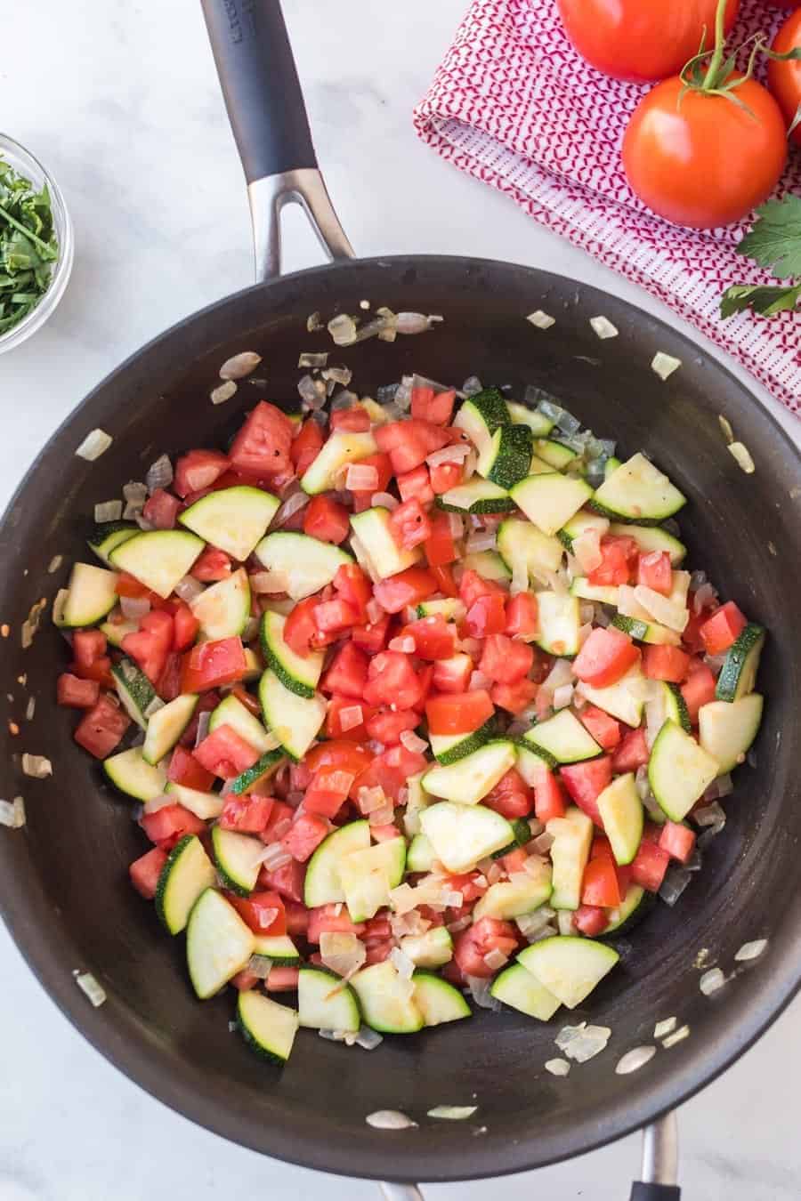 pan sautéing zucchini and tomatoes with fresh herbs.