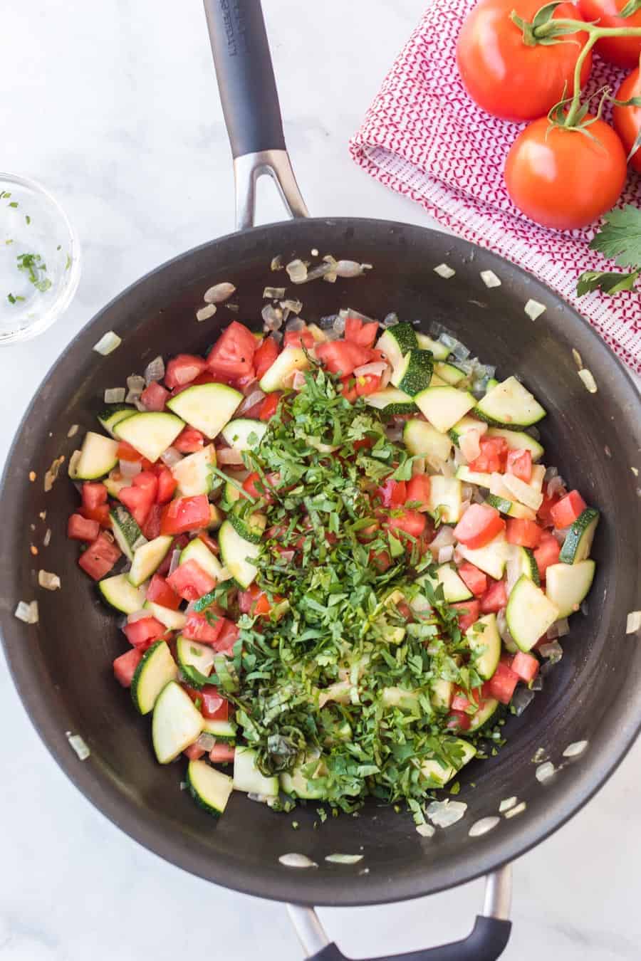 pan sautéing zucchini and tomatoes with fresh herbs.