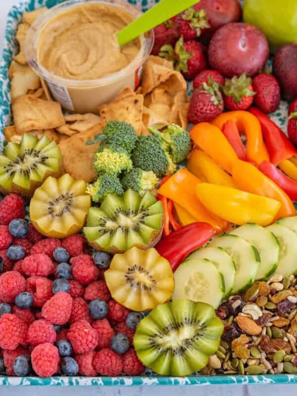 after school snack tray on a blue speckled sheet with mixed fruits, veggies, nuts, hummus and pita chips