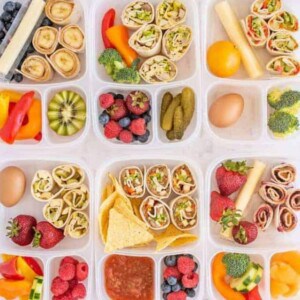 Nine lunchboxes filled with colorful, healthy foods including fruit, vegetables, cheese sticks, berries, and easy pinwheel recipes like rolled wraps and tortilla chips with salsa—all neatly arranged in compartments.
