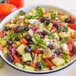 cucumber and tomato salad with olives and basil in a white bowl close up