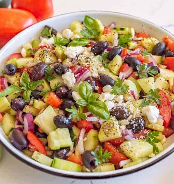 cucumber and tomato salad with olives and basil in a white bowl close up