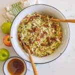 cabbage and apple salad with walnuts in a white bowl with two wooden spoons top view.