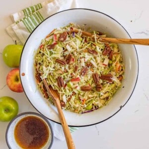 cabbage and apple salad with walnuts in a white bowl with two wooden spoons top view.