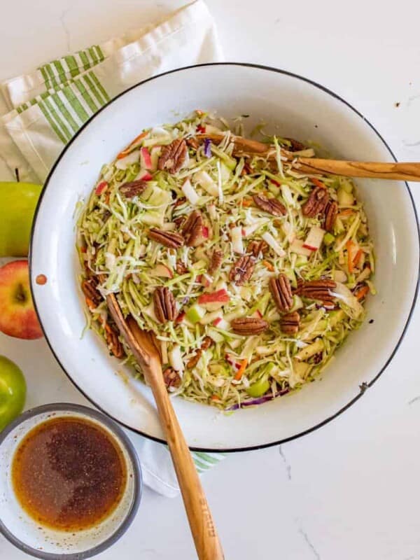 cabbage and apple salad with walnuts in a white bowl with two wooden spoons top view.