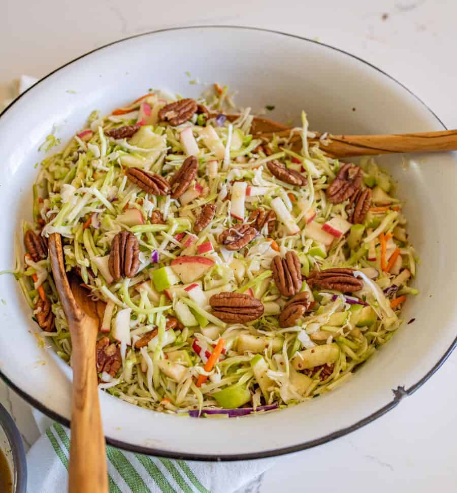 cabbage and apple salad with pecans in a white bowl with two wooden spoons.