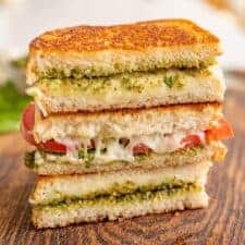 pesto grilled cheese and tomato sandwiches sliced revealing the melty inside